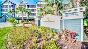 A hotel with a sign reading "PALISADES," featuring a modern building with large windows and a well-maintained garden with various plants and a red fire hydrant. - Upstay - LRG Condo w Outdoor Pool, Sauna (Winter Garden)