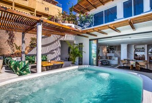 A modern outdoor pool area with a wooden pergola, seating, and a view of the interior.