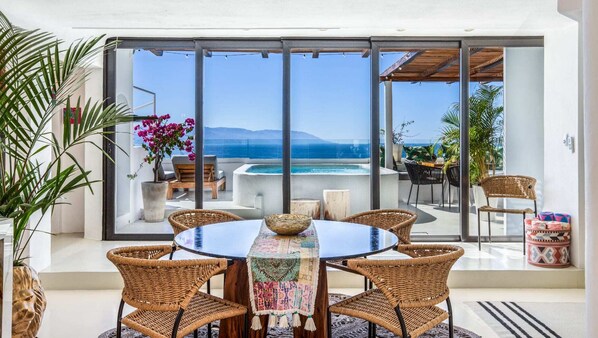 A modern outdoor dining area with a round table, wicker chairs, and a view of the sea.