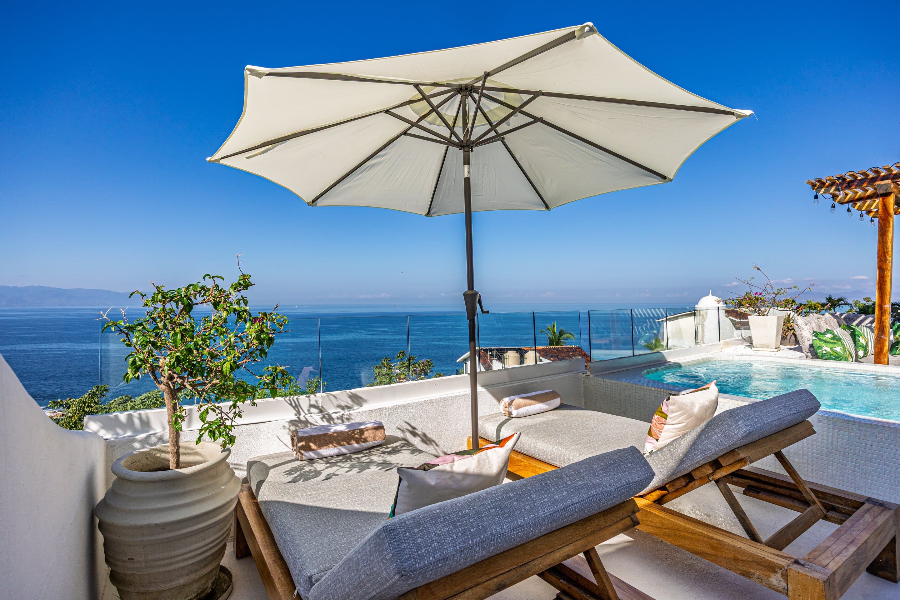 A rooftop terrace with a pool, lounge chairs, and an umbrella.