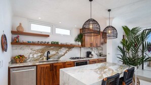 Een moderne keuken met marmeren werkbladen, houten kastjes en een centraal eiland met barkrukken.