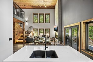 A modern kitchen with a large island, a dining area with a wooden table and chairs, and a staircase leading to an upper level. - 🛁 Hot Tub Getaway | Shuffleboard Loft, 2.2mi to Pigeon Forge (Pigeon Forge)