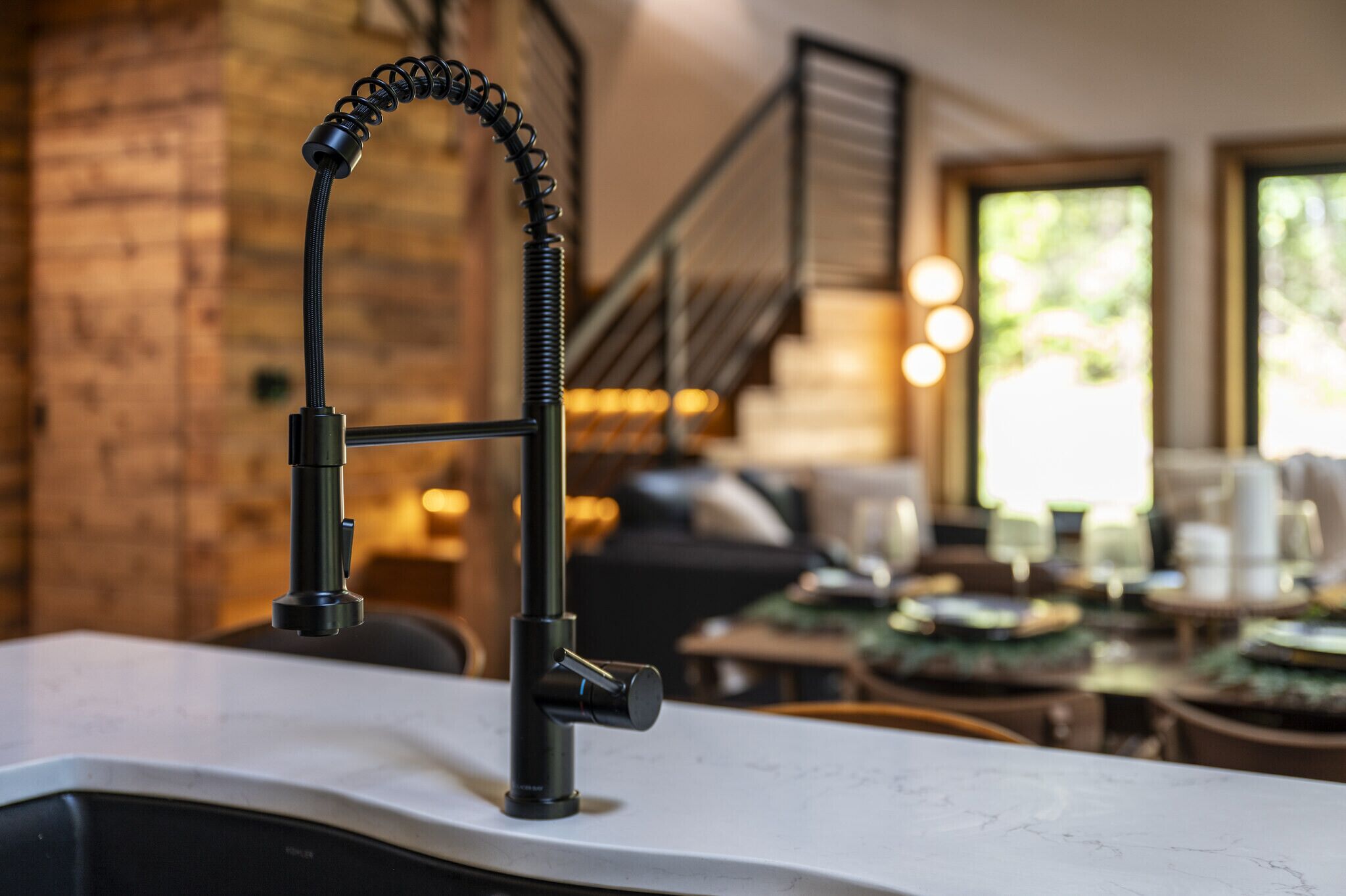 A kitchen with a modern faucet, a brick wall, and a staircase in the background.