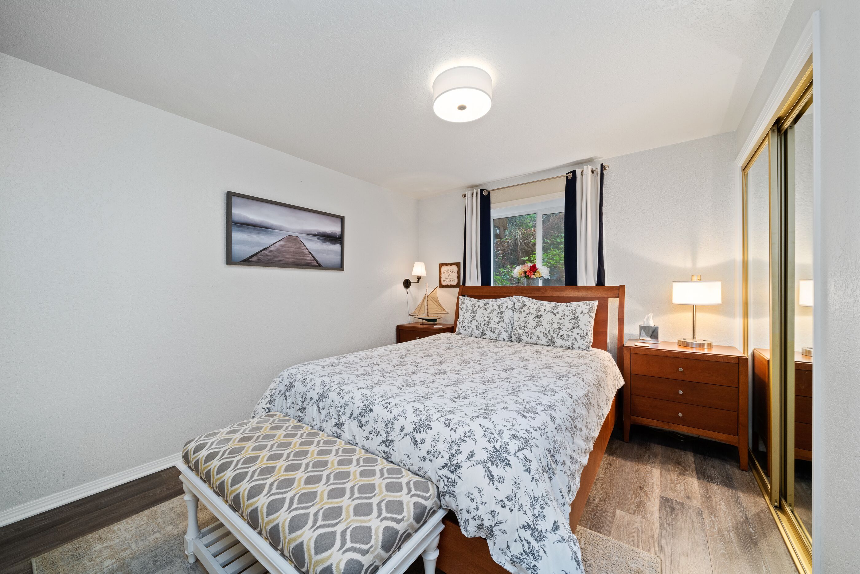 A bedroom with a bed, nightstands, a mirror, and a window with curtains.