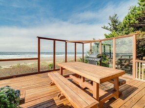 A wooden deck with a table and benches overlooking a beach and ocean.