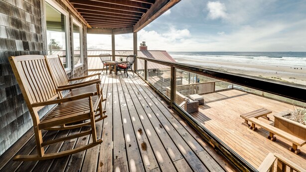 Una terraza de madera con vistas a la playa, que incluye una mesa y sillas.