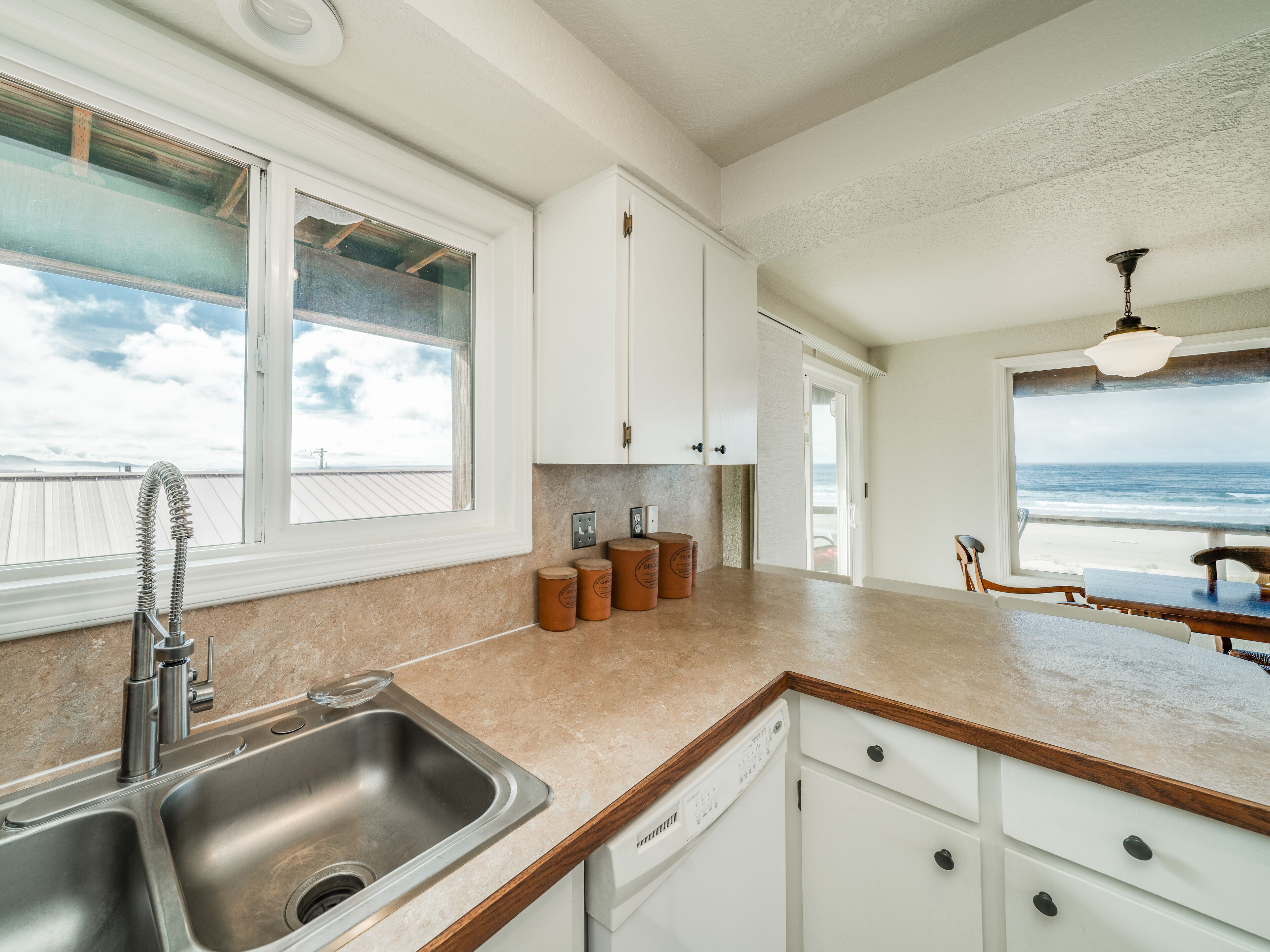 A kitchen with a view of the ocean, a sink, and wooden cabinets.