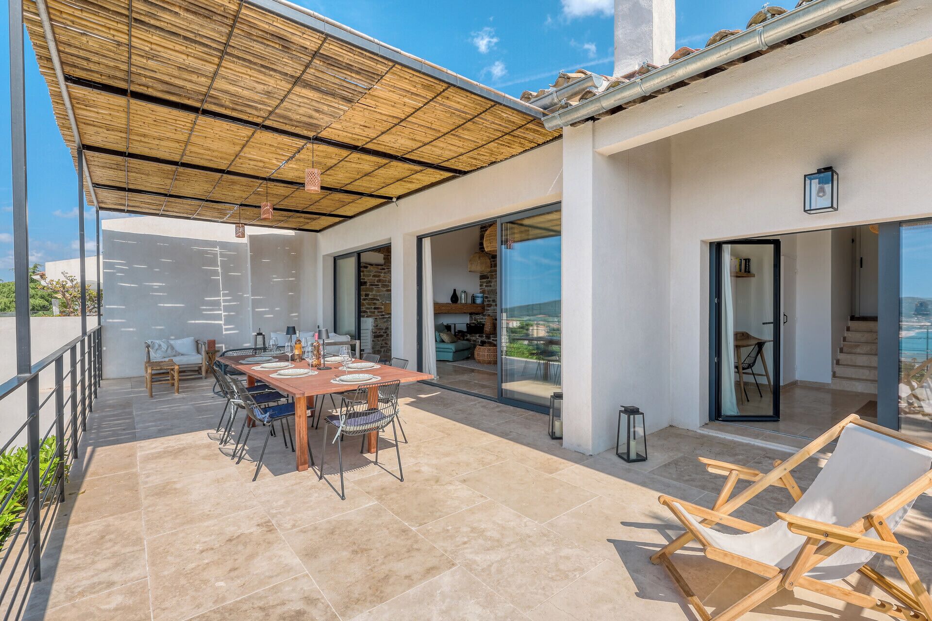 An outdoor patio with a dining table and chairs, a covered seating area, and a view of the sea.
