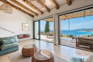 A spacious living room with a large sliding glass door leading to an outdoor terrace with a view of the sea. - Sea view villa with swimming pool for 6 people (Le Lavandou)