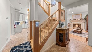 Un vaste espace de vie agrémenté d’un escalier en bois, d’une cheminée et d’une cuisine située au fond de la pièce.