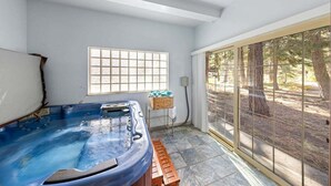 Une salle de spa équipée d’un jacuzzi, d’une fenêtre donnant sur la forêt et d’un banc en bois.