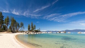En strand med kristallklart turkosfärgat vatten, en sandstrand och höga tallar.