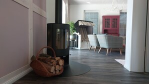 Una sala de estar moderna con un hogar a leña, sillas de mimbre, un armario rojo y un comedor con un sofá a rayas.