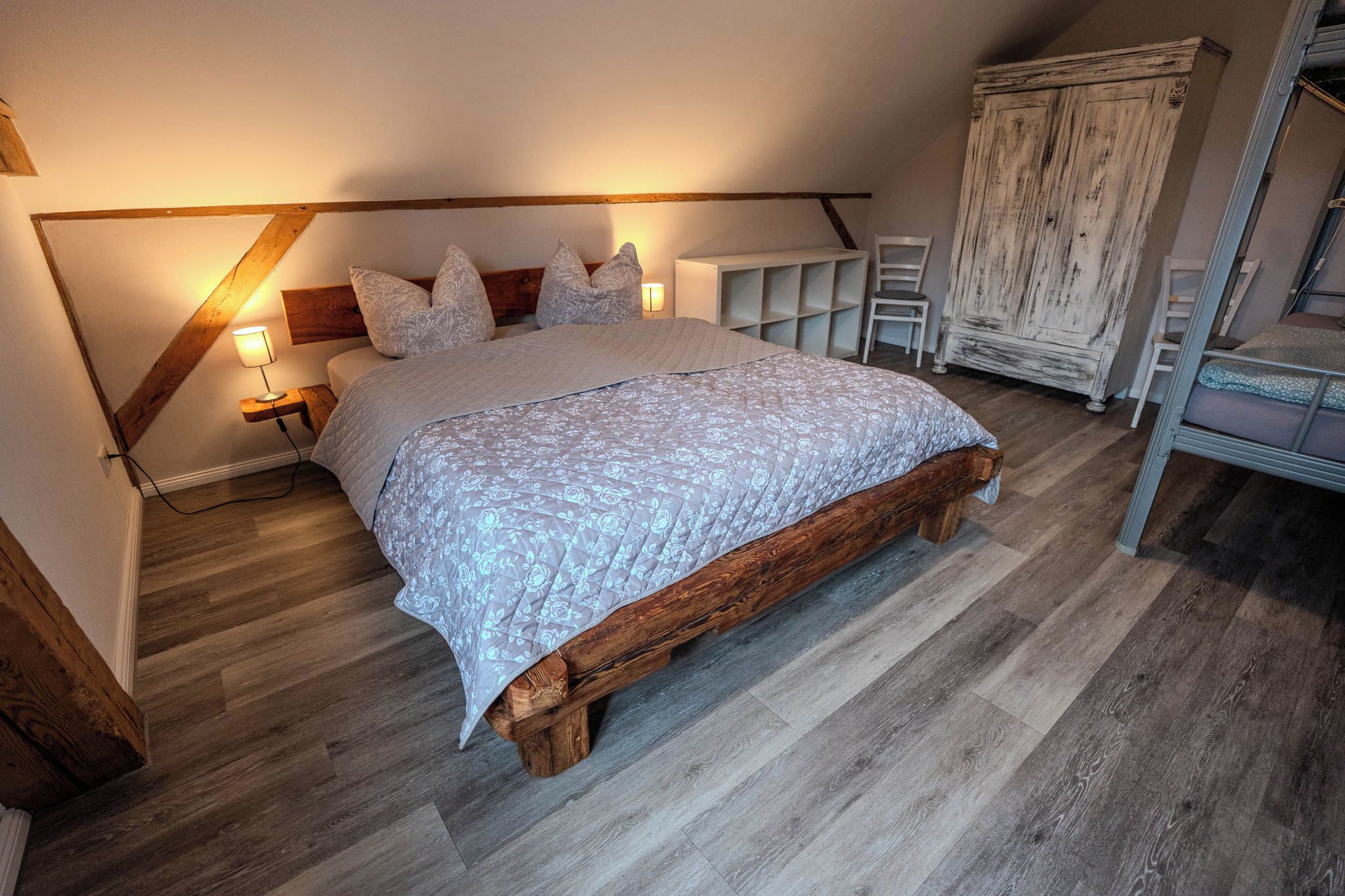 A bedroom with a wooden bed frame, a nightstand, a lamp, and a wardrobe.