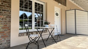 Un patio con una mesa, sillas, una planta en maceta y una puerta blanca con una placa.