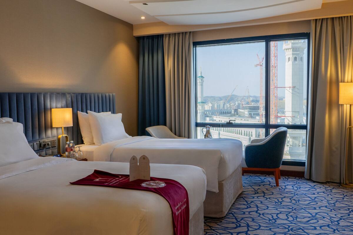 A hotel room with two beds, a view of the cityscape, and a large window with curtains.