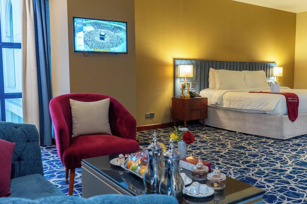 A hotel room with a bed, a red armchair, a small table with a tray of food, and a television mounted on the wall.