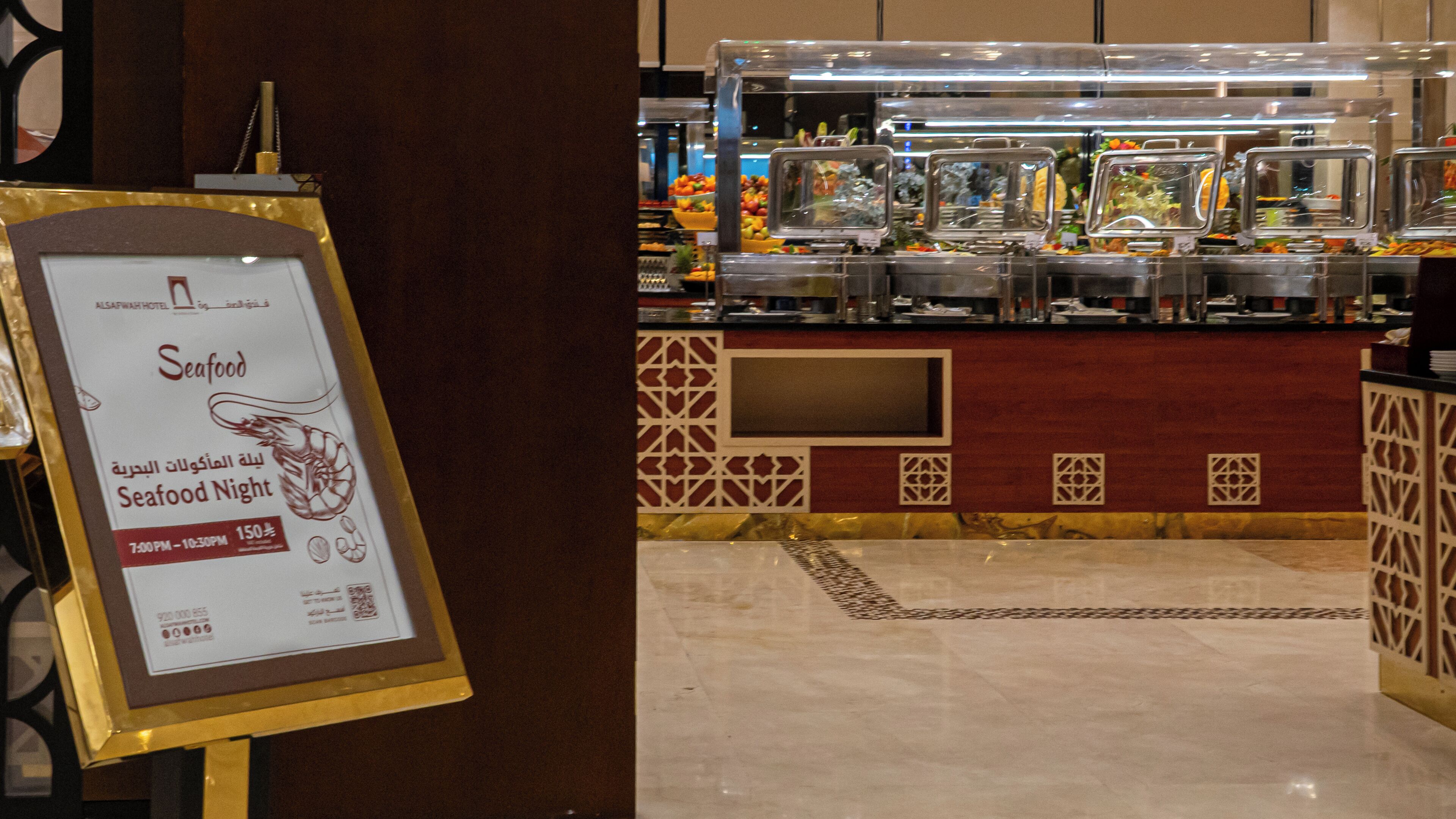 A buffet area with various food options, a sign for a Seafood Night event, and a decorative wall with geometric patterns.