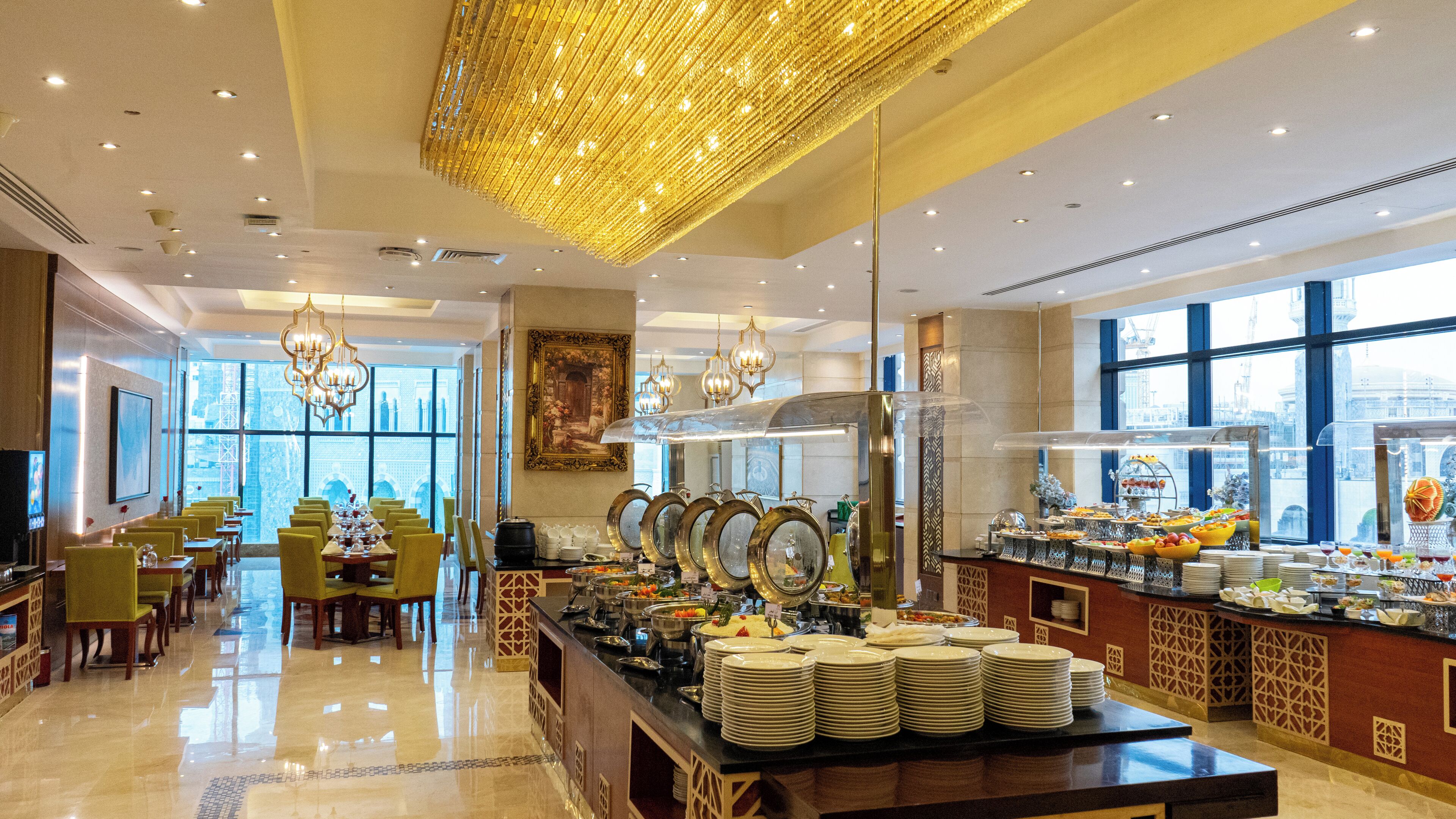 A hotel dining area with a buffet, chandeliers, and a view of the cityscape.