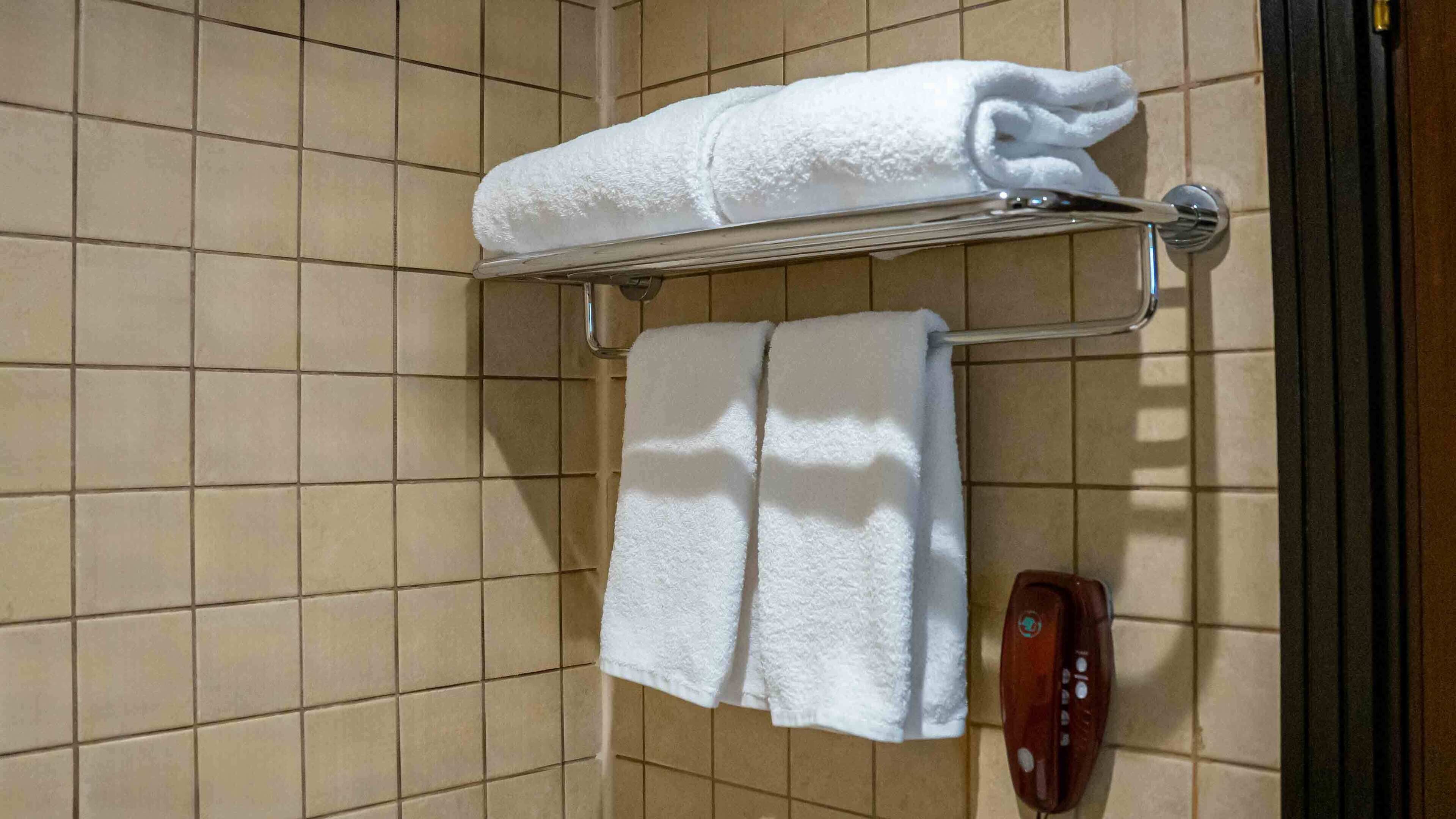 A bathroom with a towel rack holding a folded towel and a wall-mounted phone.