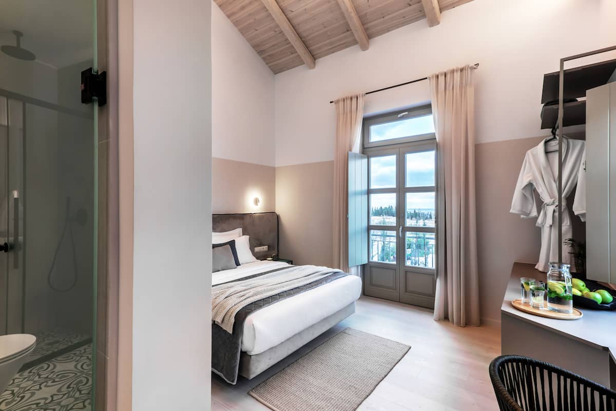 Un dormitorio moderno con una cama grande, ducha, tocador con espejo y vistas al exterior.