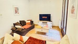 A living room with a sofa, a coffee table, and a TV displaying the Netflix logo. - Maison Paisible, 15 min du Futuroscope & Arena (Fontaine-le-Comte)