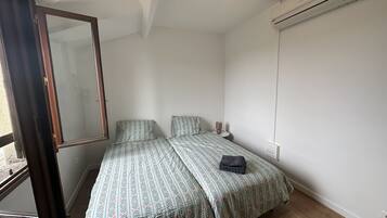 Ein kleines, ordentlich eingerichtetes Schlafzimmer mit Bett, Nachttisch, Spiegel und einer Klimaanlage.