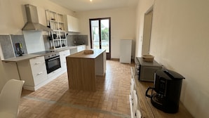 A compact kitchen with white cabinets, a central island, a built-in oven, and a coffee machine. - Maison Paisible, 15 min du Futuroscope & Arena (Fontaine-le-Comte)