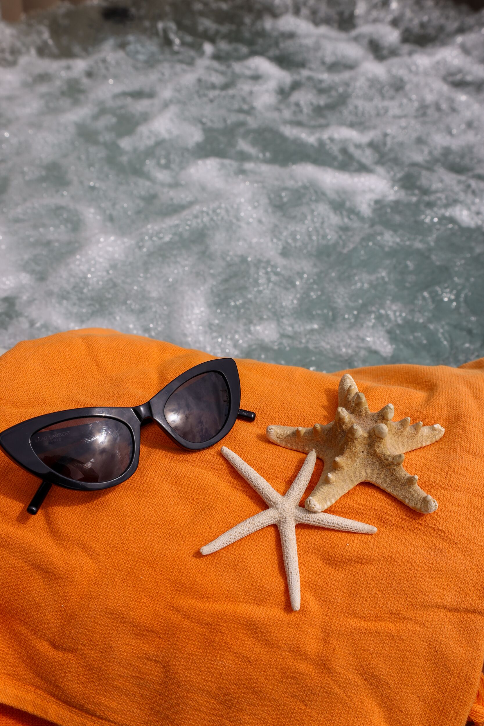 A pair of sunglasses and a starfish on an orange cloth.