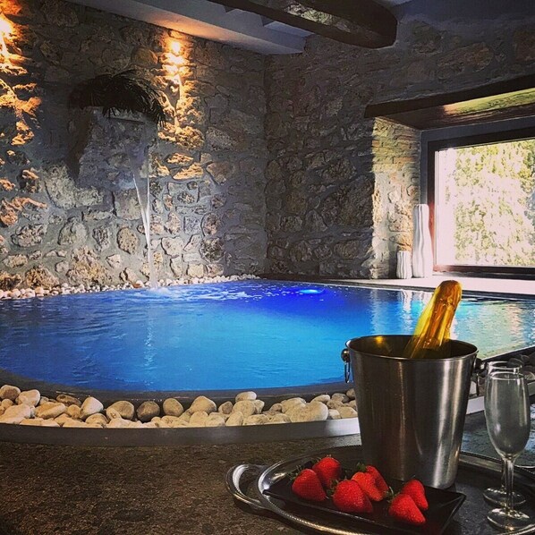 Piscina interior com paredes de pedra, balde de champanhe e morangos numa bandeja.