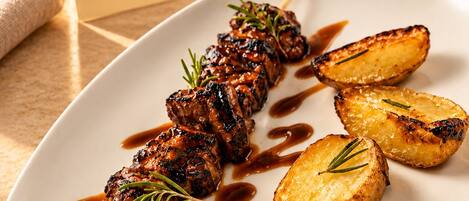 Un plato con brochetas de carne y papas asadas sobre una mesa con una tarjeta de menú.