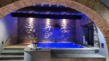 A spa area with a stone wall backdrop, a hot tub, and a set of stairs leading to the hot tub.