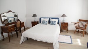 A bedroom with a large bed, two bedside tables with lamps, a wooden chair, a dresser, and a mirror. - Casa Lourival (Penalva do Castelo)