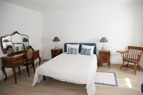 Une chambre à coucher avec un grand lit, deux tables de chevet avec des lampes, une chaise en bois, une commode et un miroir.