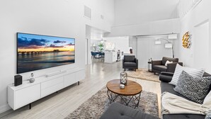 Een moderne woonkamer met een flatscreen-tv, een bank, een salontafel en een keuken in de achtergrond.