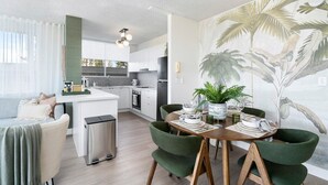A modern kitchen with white cabinets, a central island, and a dining area with green chairs. - Beachfront Bliss 2BR Broadbeach (Gold coast)