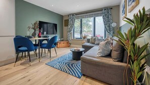 Ein modernes Wohnzimmer mit einer Couch, blauen Sesseln, einem Esstisch und einem Flachbildfernseher.
