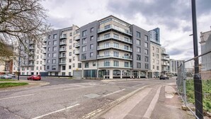Ein mehrgeschossiges Wohngebäude mit Balkonen, einem verschlossenen Eingangsbereich und einem Parkplatz.