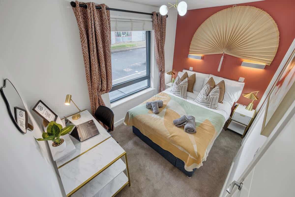 Habitación de hotel con cama, escritorio, silla y un gran ventanal con cortinas.