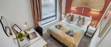 Habitación de hotel con cama, escritorio, silla y un gran ventanal con cortinas.
