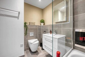 A modern bathroom with a glass shower enclosure, a white toilet, a white sink with a mirror, and a potted plant. - Stylish & Chic 1-BR Cosy Flat, City Centre Living (Southampton)