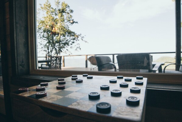 A checkered board game with pieces, a window, and a view of a balcony with chairs and a tree.