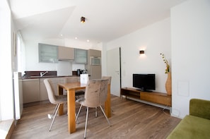 A modern kitchen with a dining area, a flat-screen TV, and a green sofa.