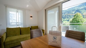 A modern living room with a wooden table, a green sofa, and a balcony with a scenic view. - Apartment Glacier View 12.6. with balcony (Kaprun)