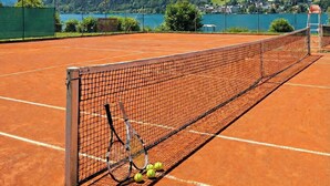 A tennis court with a net, tennis rackets, and balls, surrounded by mountains and a lake. - Apartment Glacier View 12.6. with balcony (Kaprun)