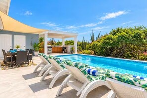 A swimming pool with lounge chairs, a covered patio area, and a dining setup. - Baby Beach Bliss Aruba | Private Pool & Outdoor Kitchen | Walk to Baby Beach (San Nicolas)