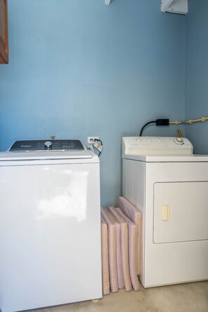 A laundry area with a front-loading washer and dryer, a hose, and a stack of folded towels. - Baby Beach Bliss Aruba | Private Pool & Outdoor Kitchen | Walk to Baby Beach (San Nicolas)