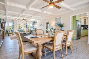 A spacious dining area with a wooden table and chairs, a ceiling fan, and a view into the kitchen.