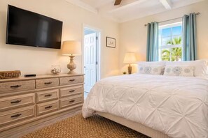 A bedroom with a bed, a dresser, a television, and a window with curtains.