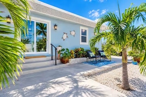 A house with a light blue exterior, a covered porch with outdoor seating, and a palm tree in the foreground.